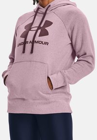 Vaaleanvioletti huppari, jossa on etutasku, mustalla Under Armour -logolla ja strukturoidulla kankaalla, jossa on pilkkuja.