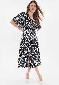 Vestido de leopardo en blanco y negro con mangas cortas y acampanadas, escote en V, cinta en la cintura y una abertura frontal, hecho de tejido ligero.