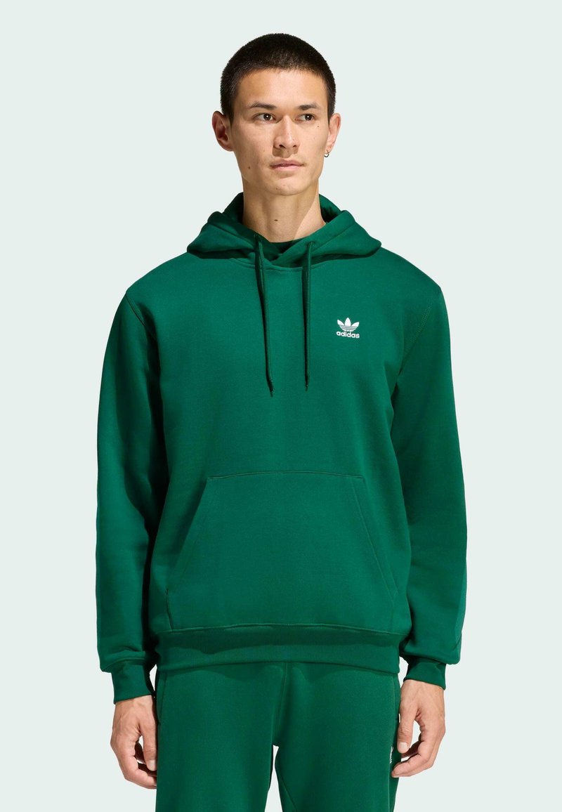 Zelená mikina s klokankou, s kapucňou na šnúrky a bielym logom Adidas na ľavej hrudi, vyrobená z mäkkej látky s hladkou štruktúrou.