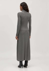 Grijze coltrui met lange mouwen, gecombineerd met een bijpassende maxi rok. De outfit is gemaakt van een zachte, rekbare stof. Zwarte hoge laarzen.