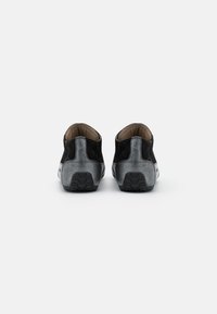 Ett par låga sneakers med svart mocka och grå texturerad häl, visande bakvy på vit bakgrund.