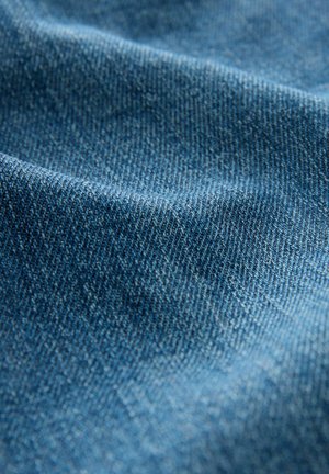 Tessuto denim di colore blu medio con una sottile texture e un motivo a trama diagonale, che mostra pieghe e grinze.