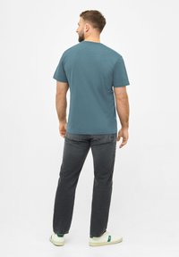 Teal korte mouwen t-shirt van zacht katoen, gecombineerd met donkergrijze jeans en witte sneakers met groene accenten. Minimalistisch ontwerp.
