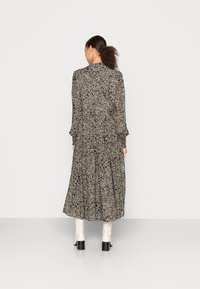 Vestido longa em tecido leve e estampado. Apresenta mangas longas, cintura ajustada e barra em camadas. Cores: bege suave e preto.