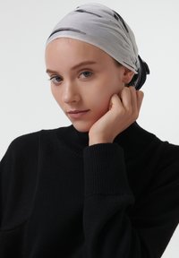 Écharpe grise légère avec des motifs abstraits noirs, portée sur la tête. Modèle portant un pull à col roulé noir, texture douce, vue en gros plan.