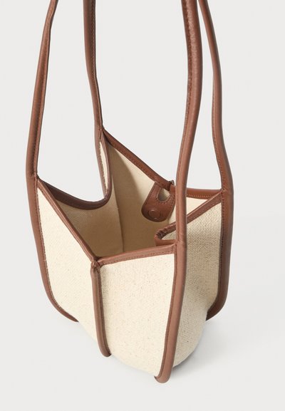 Μικρή μπεζ τσάντα υφάσματος με καφέ δερμάτινη επένδυση και μακριές λαβές, ανοιχτό πάνω μέρος με κλεισίματος με μαγνητικό κούμπωμα.