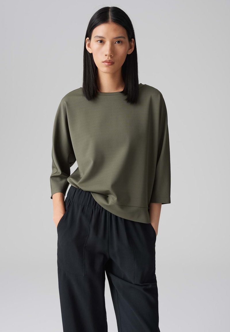 Olijfgroene, losse top met driekwart mouwen, gladde textuur, ronde halslijn, gecombineerd met zwarte, broek met elastische taille.