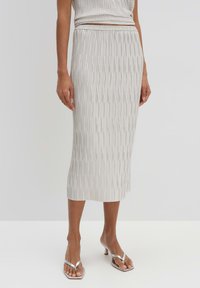 Lange pencil skirt in lichtgrijs met verticale plooien, met een elastische tailleband. Gladde textuur en lengte tot op de kuiten. Gecombineerd met zilveren sandalen.