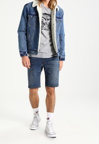Denim-takk med lammeskinnskrage, grå t-skjorte med grafikk, denim-shorts og hvite høye sneakers.