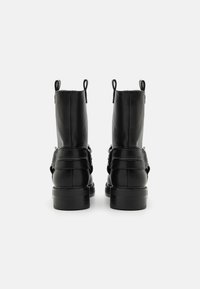 Botine negre din piele cu o textură netedă, cu bucle duble pentru tragere și curele laterale. Toc negru robust și talpă plată.