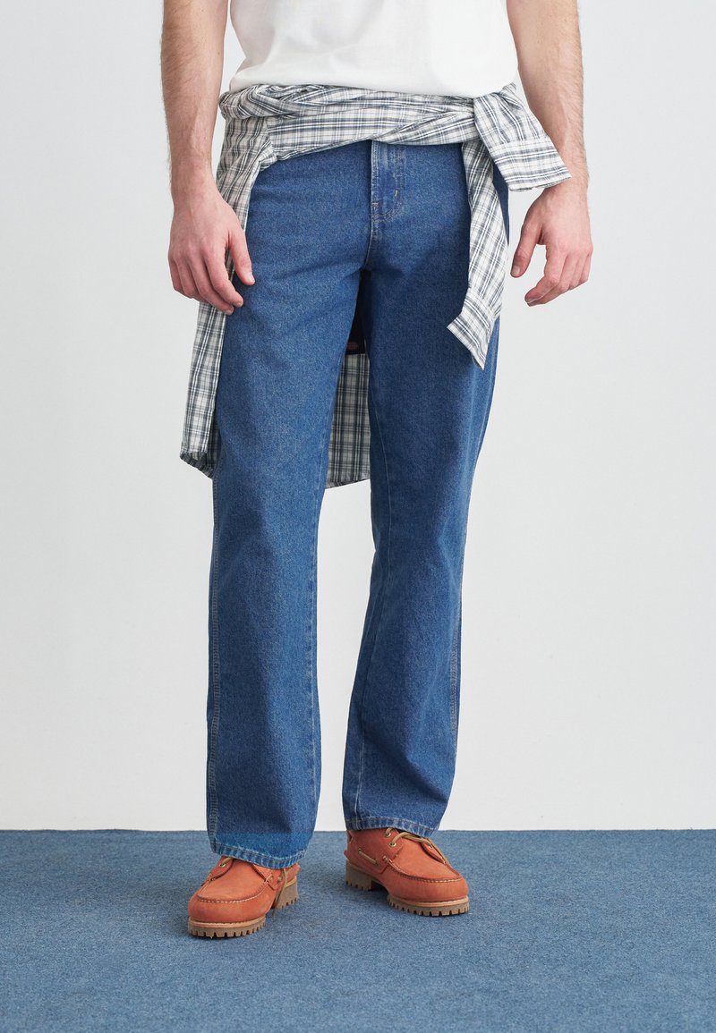 Τζιν ευθείας γραμμής σε ανοιχτό μπλε χρώμα συνδυασμένα με πορτοκαλί casual παπούτσια· ένα γκρι και λευκό καρό πουκάμισο δεμένο γύρω από τη μέση.