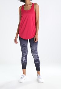 Canotta sportiva rossa abbinata a leggings neri con stampa dello skyline cittadino. L'outfit è completato da sneakers bianche.