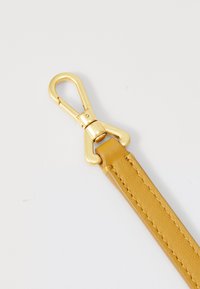 Golden metal clip attached to a textured yellow strap, showcasing a smooth finish and stitching details along the edges.