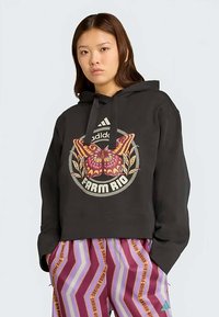 Melnas kapuces džemperis ar īsu dizainu, kurā ir krāsains tauriņš un "FARM RIO" grafika. Gluda auduma un aukliņas kapuce.