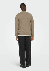 Jersey marrón de punto con cuello redondo y ribete acanalado, combinado con pantalones negros holgados y calzado oscuro, visto desde atrás.