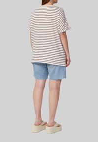 Gestreiftes, kurzärmliges Hemd in Weiß mit kastanienbraunen Streifen, kombiniert mit hellblauen Jeansshorts. Dazu werden beigen Plateau-Sandalen getragen.