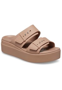 Beige platta sandaler med två justerbara remmar, silverfärgad hårdvara och en texturerad fotbädd. Tillverkad av hållbart skum material.