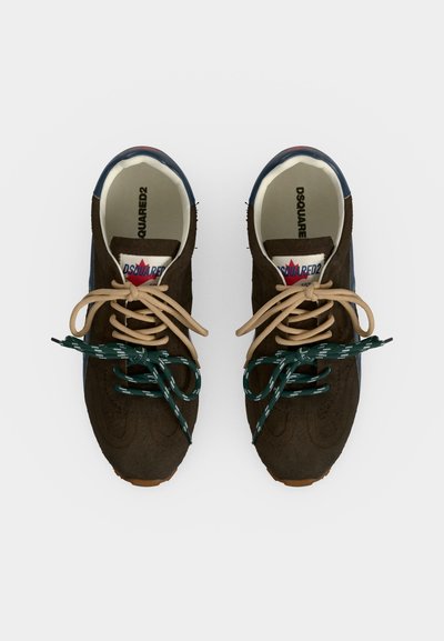 Paire de baskets marron foncé avec des lacets beige et verts dépareillés, semelles intérieures de marque et accents bleus au talon, vue de dessus sur fond blanc.