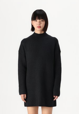 Svart strikket kjole med høy hals, oversized silhuett og ribbestrikket tekstur. Lange ermer med avslappet passform. Enkel og ensartet design.