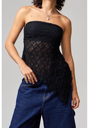 Vrouw draagt een zwarte, strapless asymmetrische kanten top gecombineerd met losse donkerblauwe jeans en een zilveren hangersketting.