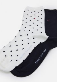 Due paia di calzini: uno bianco con pois neri, l'altro blu navy uniforme. Entrambi presentano il marchio "TOMMY HILFIGER" in testo azzurro chiaro.