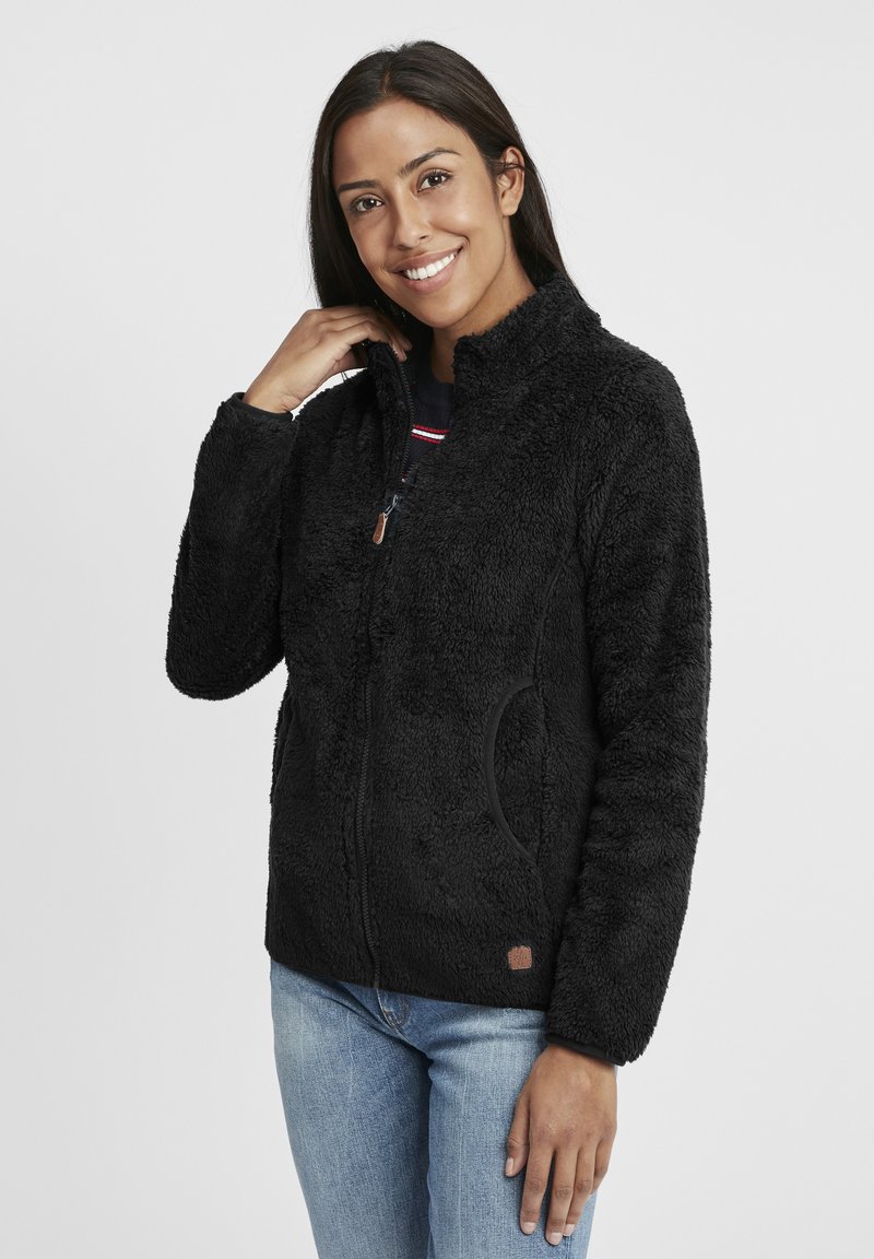 Schwarze Fleecejacke mit Reißverschluss vorne, hohem Kragen, seitlichen Taschen und strukturierter Oberfläche. Sie verfügt über ein kleines Logo am unteren Saum.