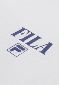 Tissu blanc avec un logo FILA bleu et un emblème carré présentant des formes "F" stylisées imprimées à la surface.