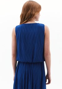 Abito plissettato blu con design senza maniche, caratterizzato da un tessuto fluido e testurizzato e una vita elastica, mostrato di schiena.