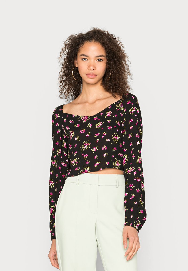 Top cropped preto com mangas longas, apresentando um padrão floral em rosa e verde. Tecido suave com um design de decote à mostra.