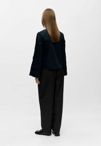 Czarny strój z długimi, szerokimi rękawami z teksturowanymi detalami po bokach, zestawiony z luźnymi czarnymi spodniami. Prosty fason.