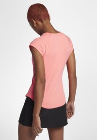 Camiseta atlética ajustada de color rosa con mangas cortas tipo cap sleeve, combinada con una falda negra. Textura suave, diseño sin costuras y dobladillo curvo en la parte trasera.