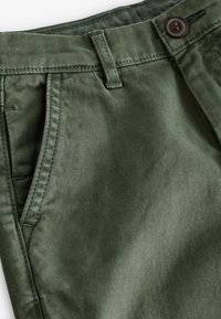 Grüne Baumwollmischungshosen mit einer glatten Textur, ausgestattet mit einem Knopfverschluss und seitlichen Taschen. Die Nähte ergänzen den Stoff.