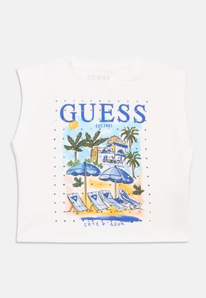 Haut blanc sans manches présentant une scène de plage avec des palmiers, des parasols bleus, des chaises longues, un hôtel et le texte « GUESS ».