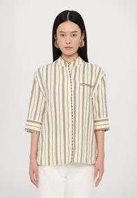 Button-up shirt in cream with black vertical stripes. Features a band collar, three-quarter sleeves, and a patch pocket.