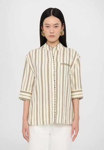 Chemise button-up crème avec des rayures verticales noires. Elle présente un col band et des manches trois-quarts, ainsi qu'une poche plaquée.
