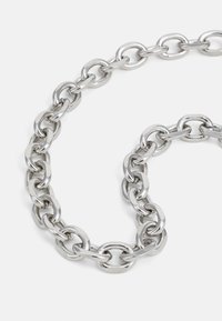 Collier en argent avec des maillons ovales de taille moyenne disposés sur un fond blanc.