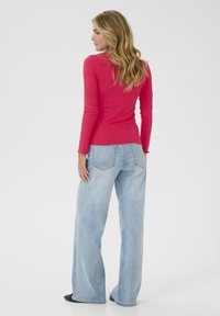 Long-sleeve, ribbed top in bright pink paired with light blue, wide-leg jeans, showcasing a relaxed fit and minimalistic design.