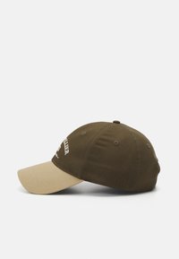 Zöld pamut baseballsapka bézs napellenzővel, díszítő varrással és hímzett szöveggel az elején. Kerek forma, állítható pánt.