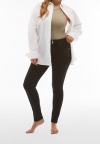 Jeans skinny negros combinados con un bodysuit beige, sobre los que se lleva una camisa de manga larga blanca sin abotonar. Tejido texturizado con acabado suave.