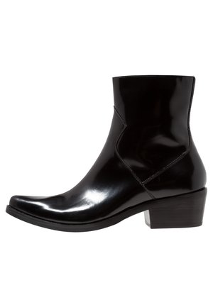 Bottine en cuir noir brillant avec bout pointu et petit talon bloc, détails de couture latérale, sur fond blanc.