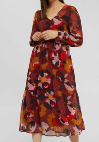 Blommönstrad klänning med djup V-ringning, långa ärmar och ett flerlagers fåll. Tillverkad av lättviktigt material i varma röda, gula och rosa nyanser.