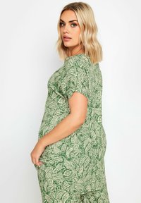 Jumpsuit verde a maniche corte con motivo a foglie su tutta la superficie, realizzato in tessuto morbido con vestibilità comoda e tasche laterali.