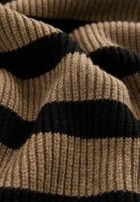 Stickad tröja med breda horisontella ränder i beige och svart. Texturerad ribbning ger djup åt ytan.