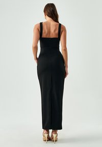 Schwarzes, figurbetontes Kleid mit einem runden Rückenausschnitt, breiten Trägern und einer langen, geraden Silhouette. Glatter Stoff mit einem verdeckten Reißverschluss auf der Rückseite.