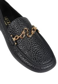 Czarne teksturowane skórzane lordsy z złotym metalowym detalem na górze, okrągłym noskiem i gładkim czarnym wykończeniem na krawędzi.