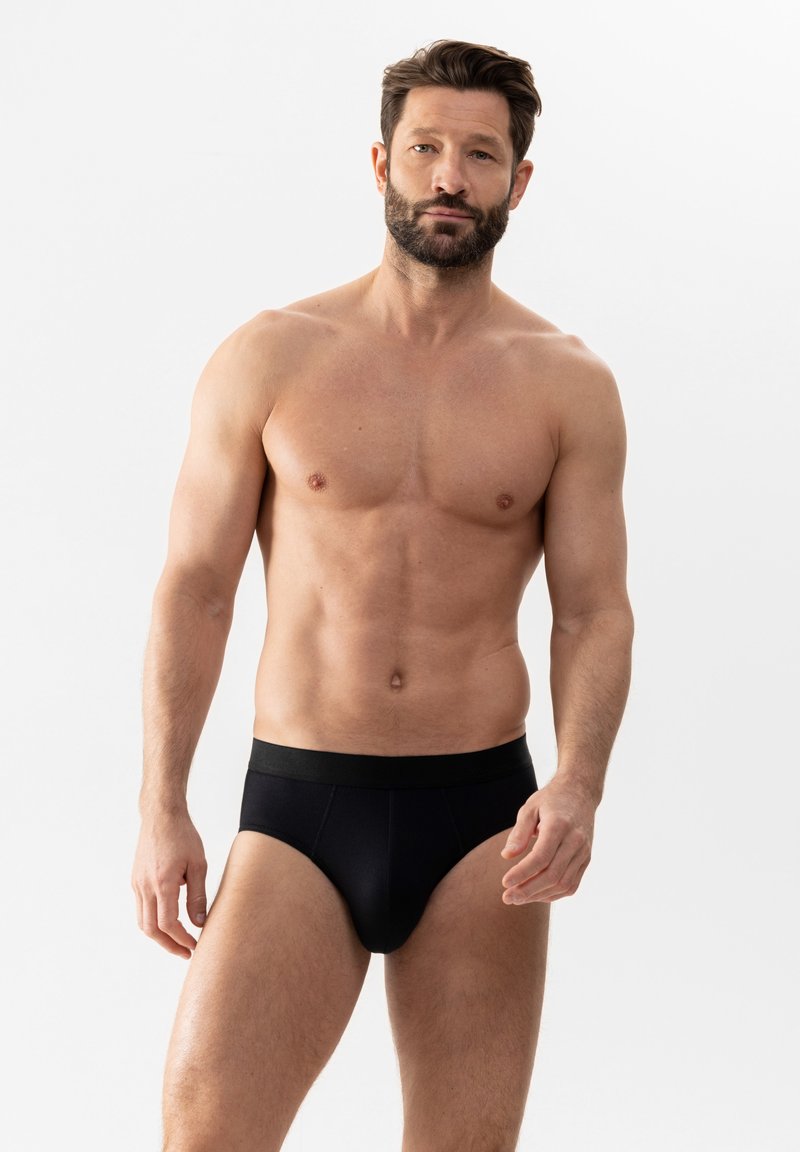 Schwarze Baumwoll-Slips mit einem breiten elastischen Bund, die eine glatte Textur und eine eng anliegende Passform aufweisen, gezeigt an einem oberkörperfreien männlichen Modell.