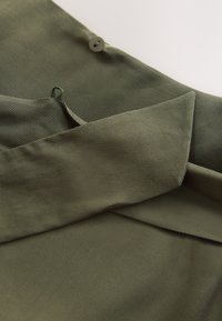 Olive green fabric featuring a ribbed texture, folded collar, and a button detail. Soft material with a smooth finish, suitable for clothing.