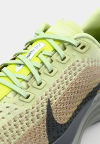 Svetlozelená bežecká obuv Nike s priedušným zvrškom a ružovými a sivými doplnkami, okrúhlymi šnúrkami a odpruženou podrážkou pre pohodlie.