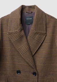 Doppelt gefütterte, braun karierte Blazer aus strukturiertem Stoff. Merkmale sind breite Revers und zwei schwarze Knöpfe an der Vorderseite. Das Markenlabel ist sichtbar.
