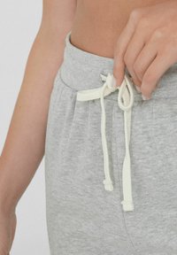 Grijze sweatpants met een zachte textuur, voorzien van een witte trekkoord dat in een strik is geknoopt bij de tailleband. Close-up van het taillegebied.